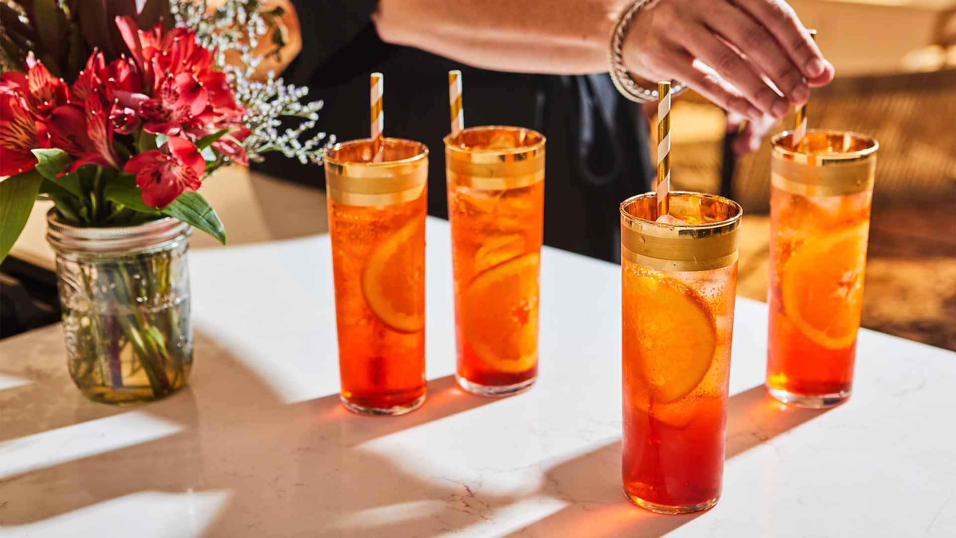 a person pouring a drink from a pitcher into four glasses
